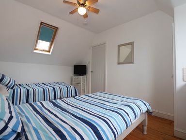 A bedroom with two beds with striped blue bedding a small TV on a white cabinet a ceiling fan and a skylight window at Angorfa Bach in Abersoch
