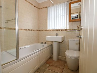 A bathroom with a bathtub shower sink toilet and a window with blinds at Angorfa Bach in Abersoch