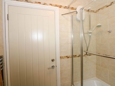 A shower area with a glass door and an electric shower unit next to a closed door in a tiled bathroom at Angorfa Bach in Abersoch