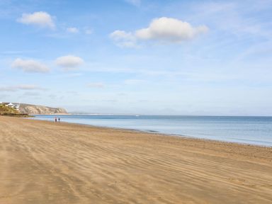 A sandy beach with two people walking near the water at Angorfa Bach in Abersoch
