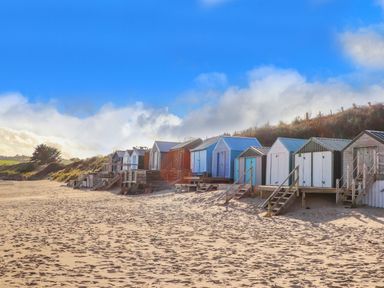 A row of small beach huts on a sandy beach with grassy hills behind them at Angorfa Bach in Abersoch