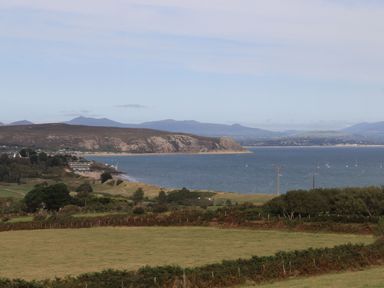 A coastal landscape with fields and hills overlooking a bay with boats at Angorfa Bach in Abersoch