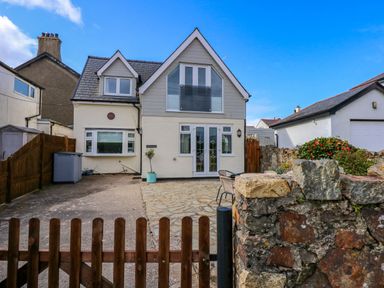 A two-story house with a wooden gate driveway and stone wall with flowers at Angorfa Bach in Abersoch