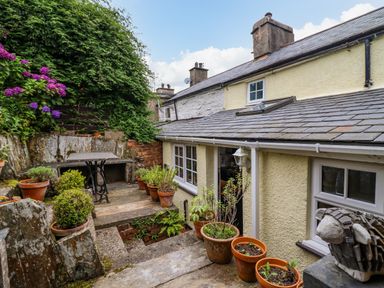 A stone patio with potted plants and a table outside a yellow stone house at Preswylfa in Ffestiniog