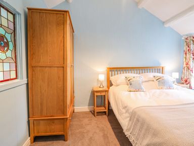 A bedroom with a wooden wardrobe bed bedside tables and a stained glass window at Preswylfa in Ffestiniog