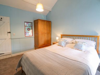 A bedroom with a double bed two pillows a wooden wardrobe a bedside table with a lamp a hanging ceiling lamp and a stained glass window at Preswylfa in Ffestiniog