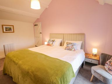 A bedroom with a double bed green blanket pillows a bedside table lamp an armchair and a painting on the wall at Preswylfa in Ffestiniog