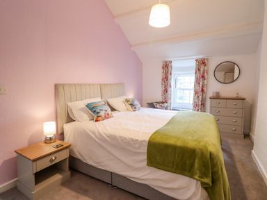 A bedroom with a double bed bedside table with lamp a chest of drawers and floral curtains at Preswylfa in Ffestiniog