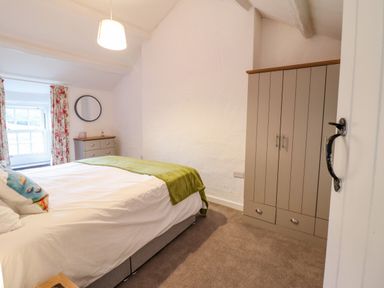 A bedroom with a bed green blanket floral curtains a dresser with a mirror and a wardrobe at Preswylfa in Ffestiniog