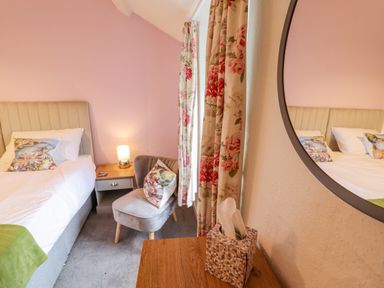 A bedroom with a bed bedside table lamp chair floral curtains and a round mirror at Preswylfa in Ffestiniog
