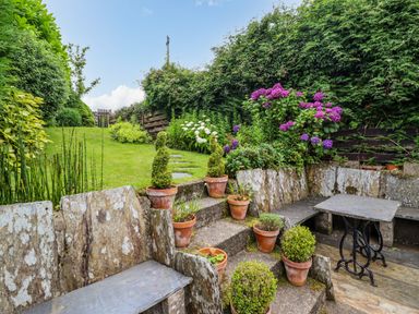 A garden with stone benches tables potted plants and a grass lawn at Preswylfa in Ffestiniog