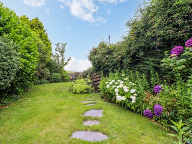 A garden path with stepping stones leading to a wooden gate surrounded by bushes and flowers at Preswylfa in Ffestiniog