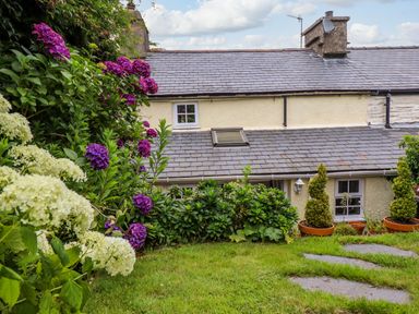 A garden with blooming flowers and shrubs in front of a cottage with a tiled roof at Preswylfa in Ffestiniog
