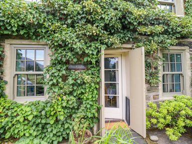 The exterior of a stone house with two windows an open door and ivy growing on the walls at Preswylfa in Ffestiniog