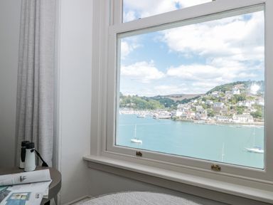 A window with a view of boats on water and houses on hills with curtains and binoculars on a table at Upper Tremorvah in Dartmouth