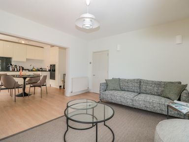 A living room with a sofa and glass tables connected to a dining area with a round table and chairs at Upper Tremorvah in Dartmouth