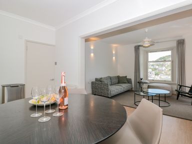 A dining area with a table set with wine glasses and a bottle looking into a living room with sofa and window at Upper Tremorvah in Dartmouth