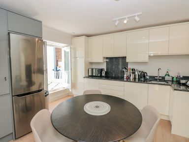 A kitchen with a round dining table chairs a stainless steel refrigerator white cabinets and a window door open at Upper Tremorvah in Dartmouth