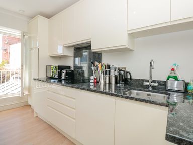 A kitchen with white cabinets black countertop a sink microwave toaster kettle and utensils at Upper Tremorvah in Dartmouth
