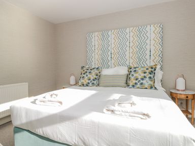 A bedroom with a double bed with patterned cushions and headboard and two bedside tables with lamps at Upper Tremorvah in Dartmouth