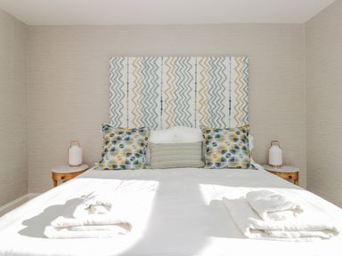 A bedroom with a bed featuring patterned cushions and headboard two bedside tables with lamps and folded towels on the bed at Upper Tremorvah in Dartmouth