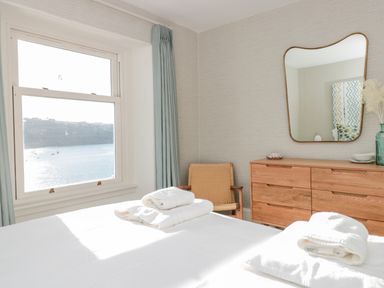 A bedroom with a window showing a water view a wooden dresser a mirror a chair and white towels on a bed at Upper Tremorvah in Dartmouth