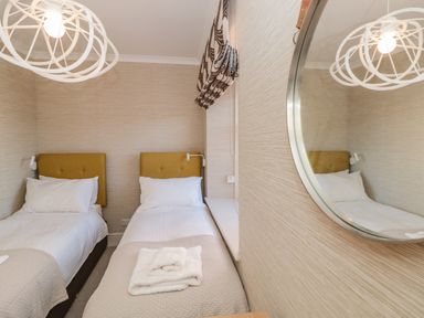 A bedroom with two single beds white bedding yellow headboards and a round wall mirror at Upper Tremorvah in Dartmouth