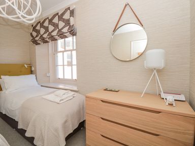 A bedroom with a single bed next to a window and a wooden dresser with a lamp and round mirror at Upper Tremorvah in Dartmouth