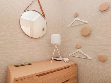 A corner with a wooden dresser a round mirror a white lamp a small figurine two white hangers on wooden wall hooks at Upper Tremorvah in Dartmouth