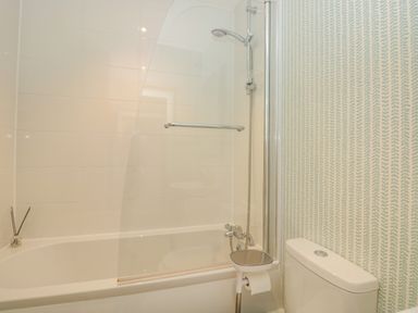 A bathroom with a bathtub shower combination a toilet and patterned wallpaper at Upper Tremorvah in Dartmouth