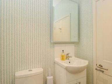 A bathroom with a toilet, a sink with cabinets, a wall mirror, and a door at Upper Tremorvah in Dartmouth