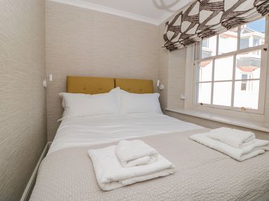 A bedroom with a double bed white sheets folded towels on the bed and a window with patterned blinds at Upper Tremorvah in Dartmouth