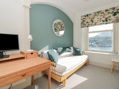 A room with a wooden desk, computer monitor, lamp, and a wooden framed sofa with cushions and a blanket at Upper Tremorvah in Dartmouth