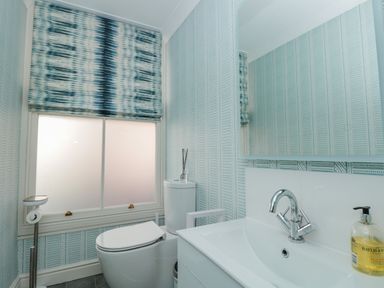 A bathroom with a toilet sink mirror window with blind and soap dispenser at Upper Tremorvah in Dartmouth