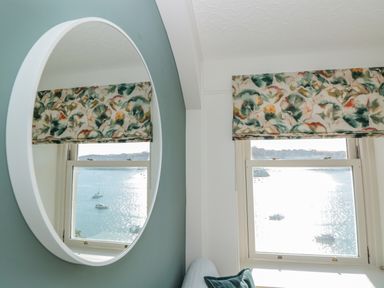 A window with a floral curtain and a view of boats on water reflected in a round mirror at Upper Tremorvah in Dartmouth