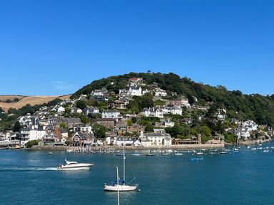 A hillside covered with houses and trees overlooking a body of water with boats in Dartmouth
