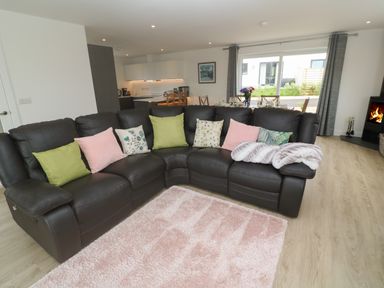 A living room with a brown leather sectional sofa and colorful cushions near a pink rug and a fireplace at 3 Praa Cove in Praa Sands