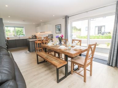 A dining area with a wooden table set for six and an open kitchen with stools at 3 Praa Cove in Praa Sands