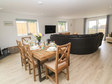 A dining table set with dishes and bottles and a large black sectional sofa in a living room at 3 Praa Cove in Praa Sands