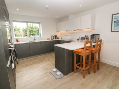 A kitchen with dark lower cabinets white upper cabinets a window and wooden bar stools at 3 Praa Cove in Praa Sands