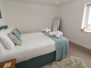 A bedroom with a double bed with pillows and towels a full-length mirror and a window with a toy bird on the sill at 3 Praa Cove in Praa Sands