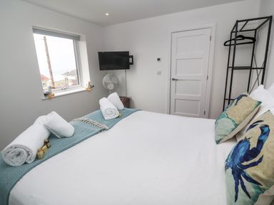 A bedroom with a bed with crab pillows a folded towel and a wall mounted TV at 3 Praa Cove in Praa Sands