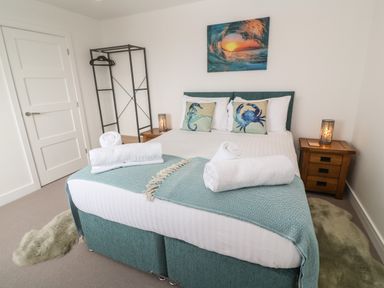 A bedroom with a double bed with rolled towels and sea creature pillows beside nightstands and a metal clothes rack at 3 Praa Cove Praa Sands