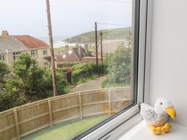 A view of houses and a seaside landscape through a window with a stuffed bird on the windowsill at 3 Praa Cove in Praa Sands