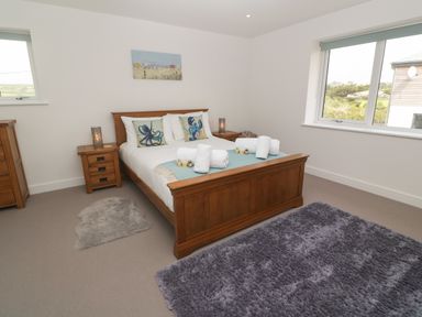 A bedroom with a wooden double bed two bedside tables two rugs and windows in a house at 3 Praa Cove in Praa Sands