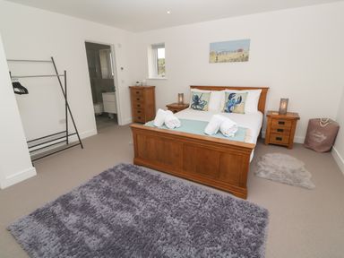 A bedroom with a wooden bed, two nightstands, chest of drawers, rugs, and a clothes rack at 3 Praa Cove in Praa Sands