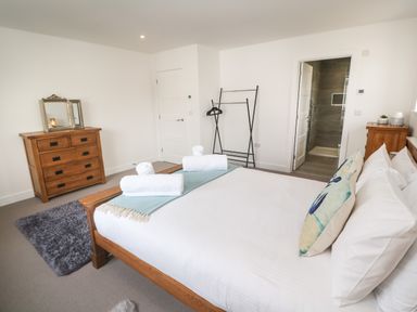A bedroom with a wooden bed and dresser white walls a rug and an open door to a bathroom at 3 Praa Cove in Praa Sands