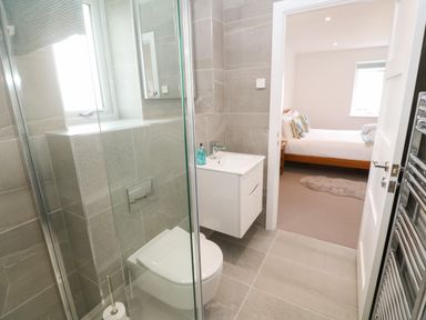 A bathroom with a toilet, sink, shower, and a view into a bedroom with a bed and window at 3 Praa Cove in Praa Sands