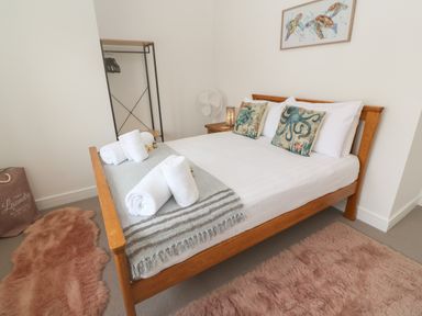 A bedroom with a wooden bed with white linens and sea animal pillows beside a metal open wardrobe and fluffy rugs at 3 Praa Cove in Praa Sands