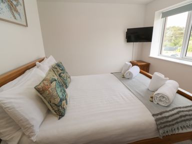 A bedroom with a double bed two decorative pillows rolled towels a television and a window at 3 Praa Cove in Praa Sands